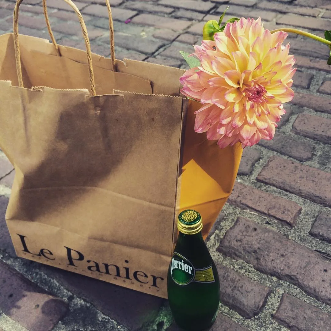 A bag from pike place market's le panier with a flower and bottled water.
