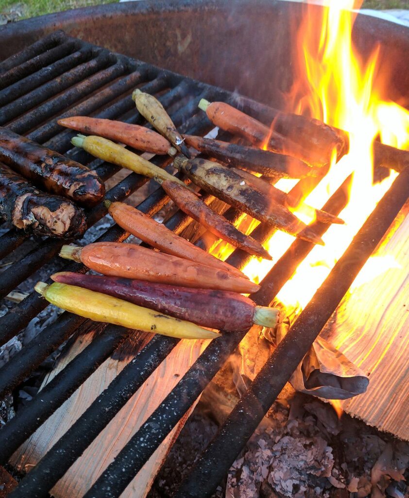 Carrots and sausages cooking over an open fire.
