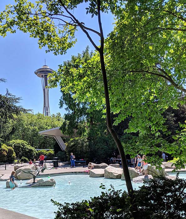 The space needle as seen behind a wading friendly fountain