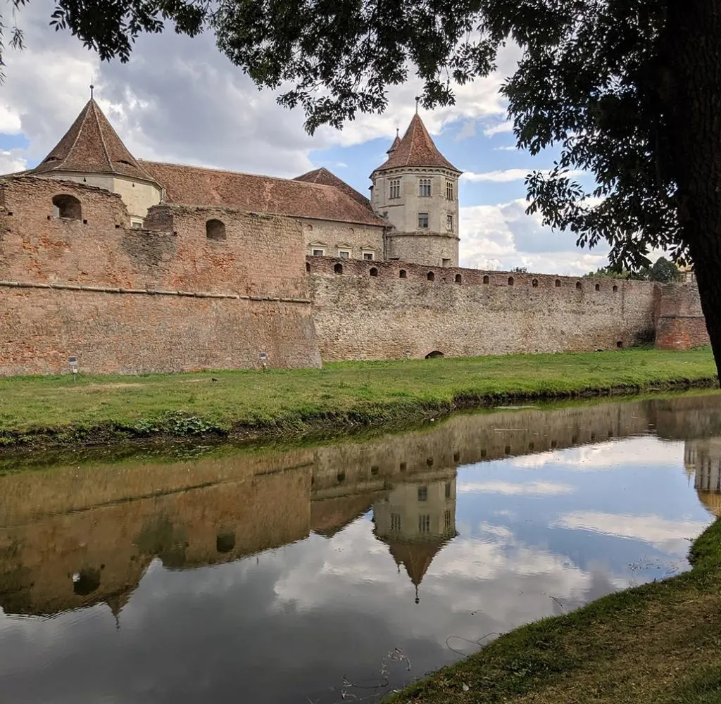 Castle walls and moat in fagaras, set against a cloudy blue sky in romania