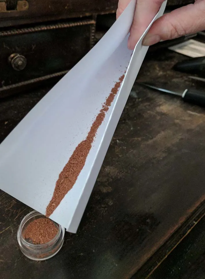 Pouring eyeshadow into a travel sized container.