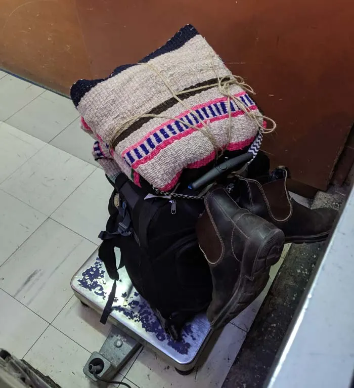 A small carry-on bag with a souvenir blanket on top of a scale at a bus station