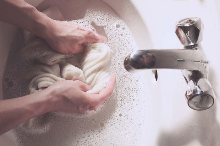 Hands washing white knit socks in a sink during travel laundry washing