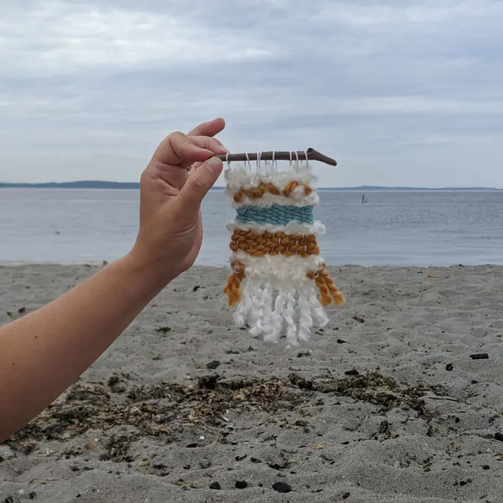 A tiny handmade weaving being held up on a beach.