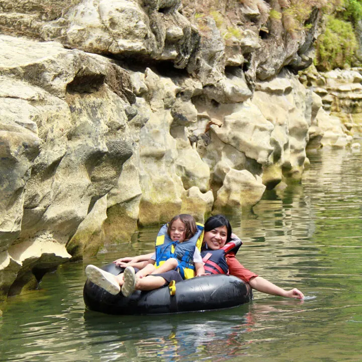 An adult and child float past a rock formation on an inflatable tube.
