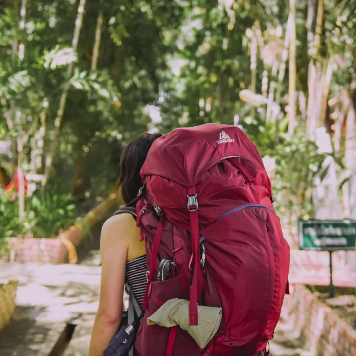 A woman with a large backpack walks in a forested area.