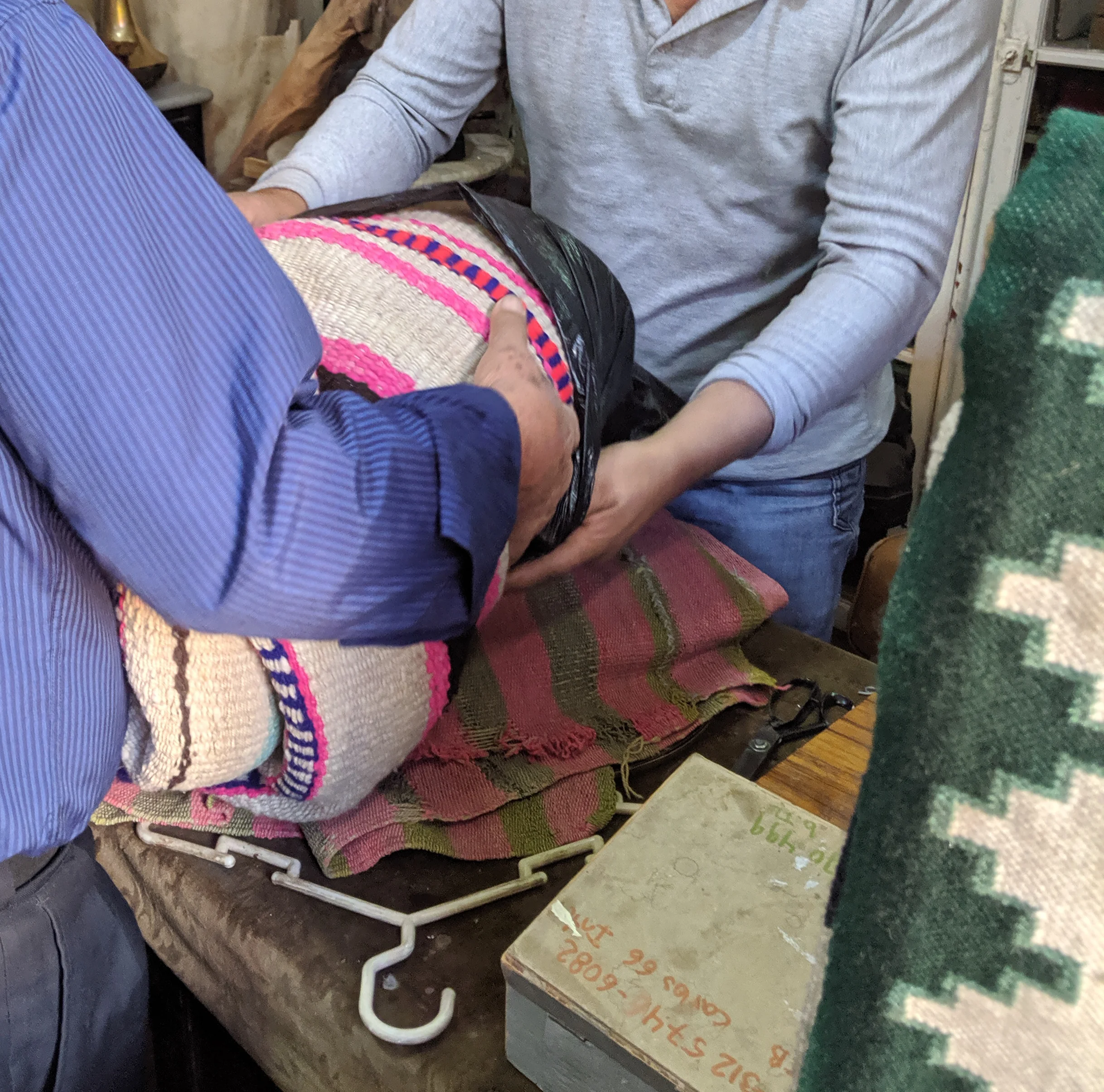 Two men place a frazada in a bag.