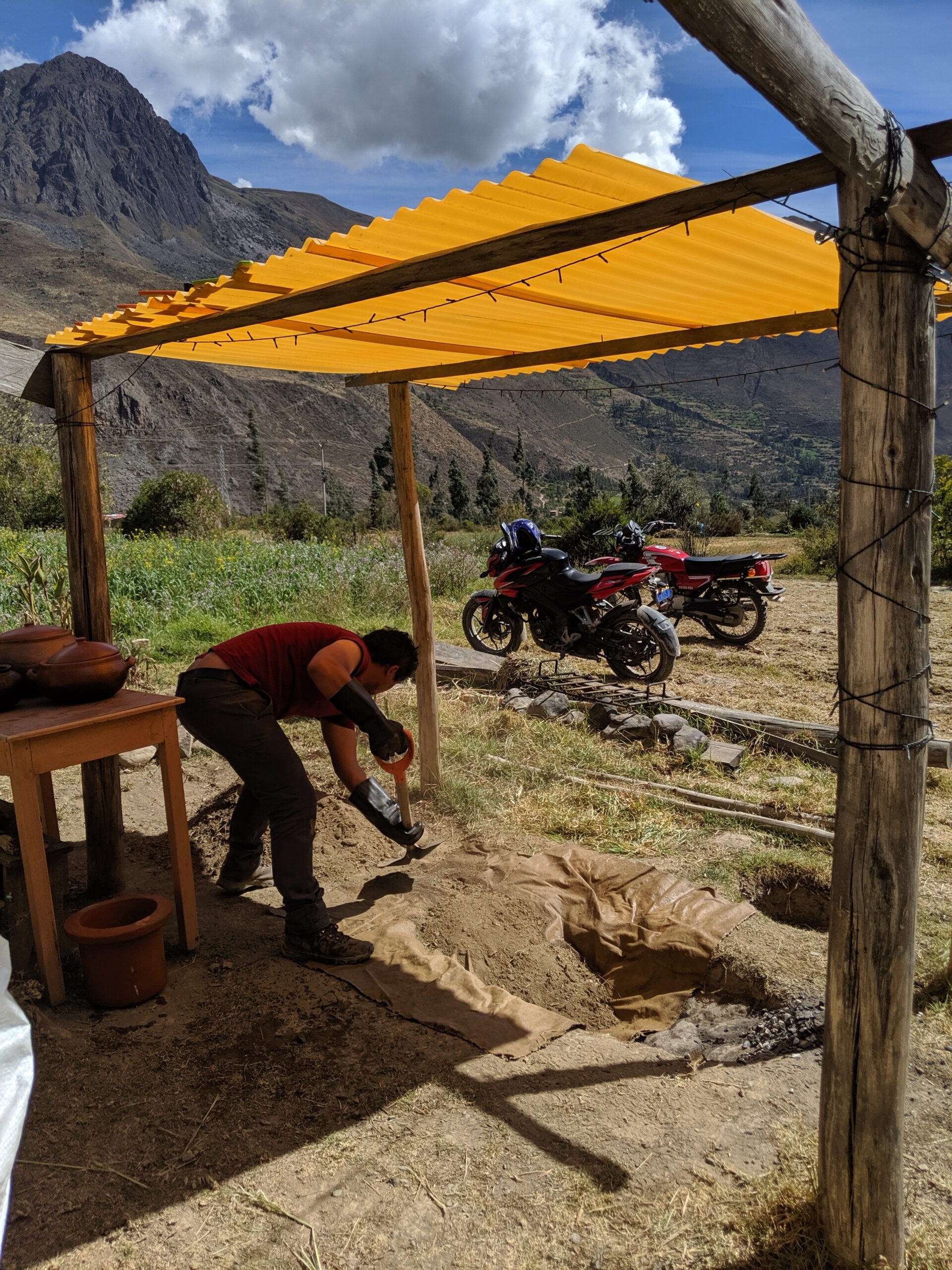 A man covers an underground oven for cooking.