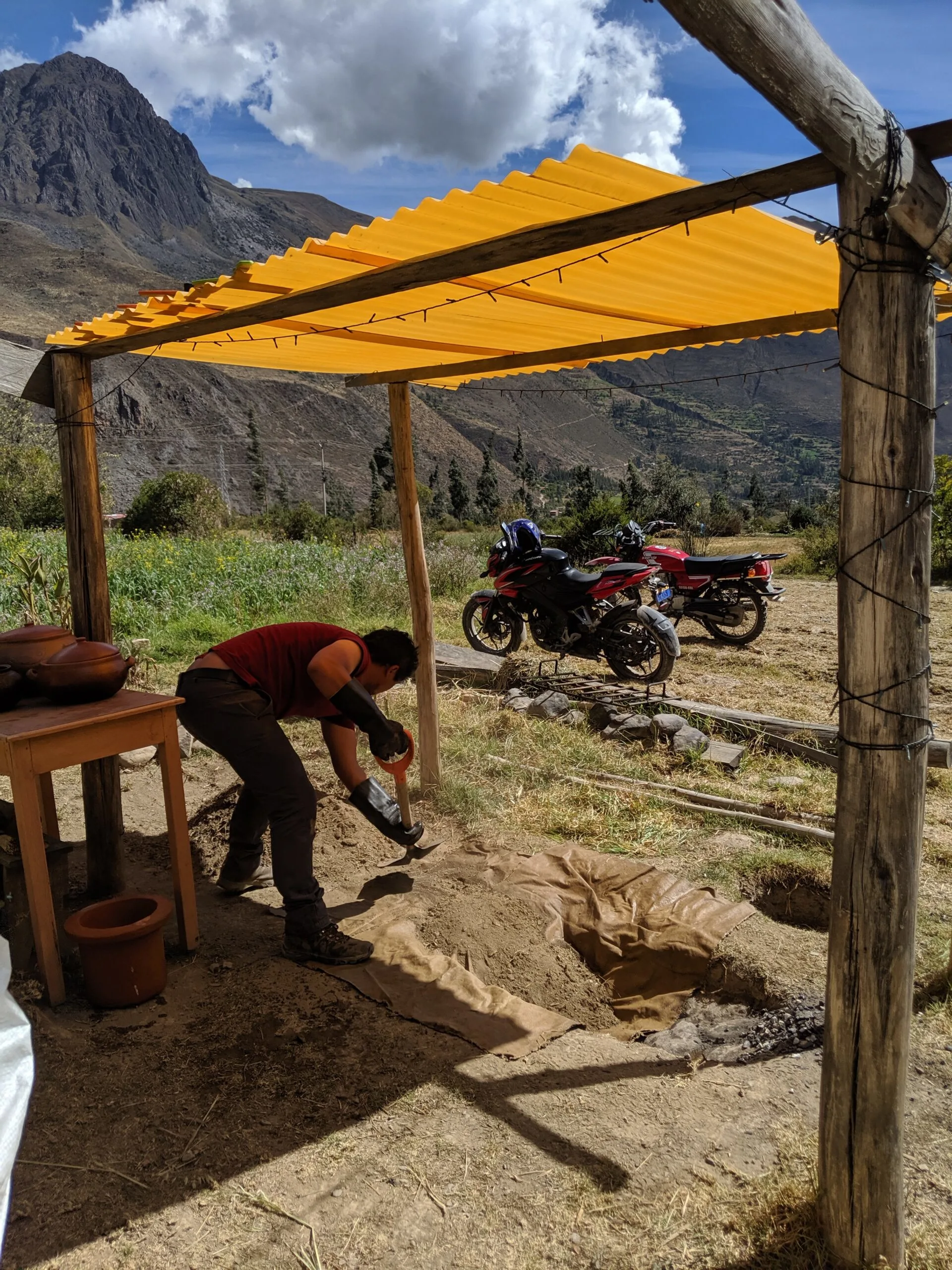 A man covers an underground oven for cooking.