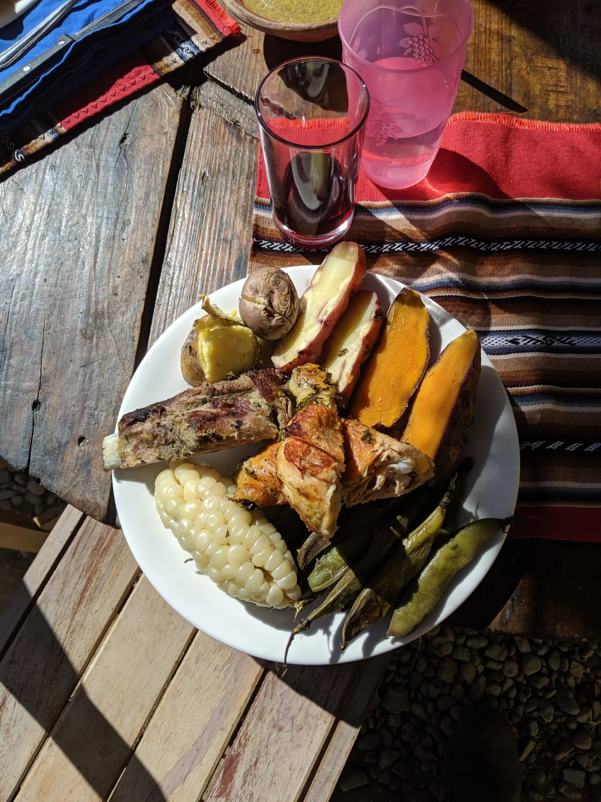 A plate of traditional peruvian meal called a pachamama, containing several kinds of potatoes, chicken, corn, beef ribs, and beans.