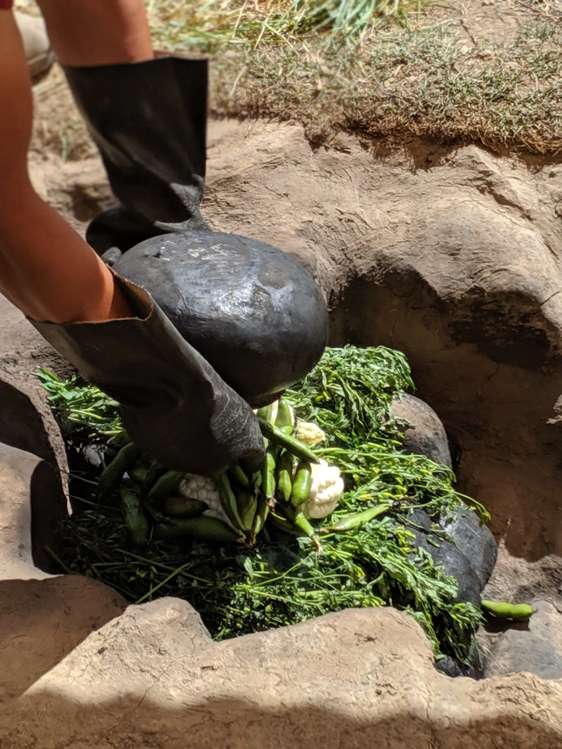 Close-up of a man placing rocks onto a meal cooked in the ground.