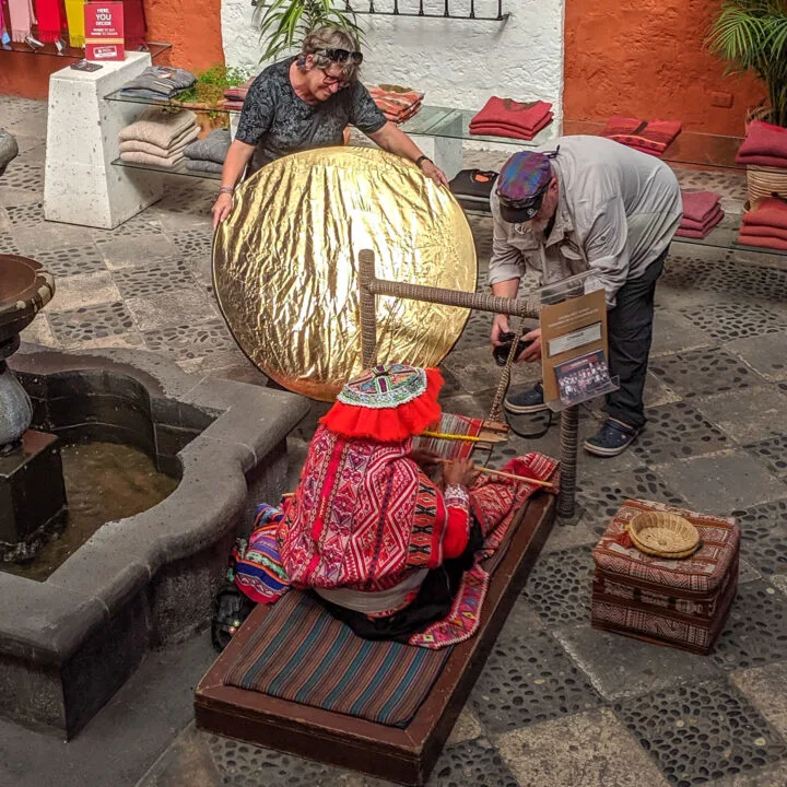 Two western tourists use professional equipment to photograph a indigenous woman in Peru.