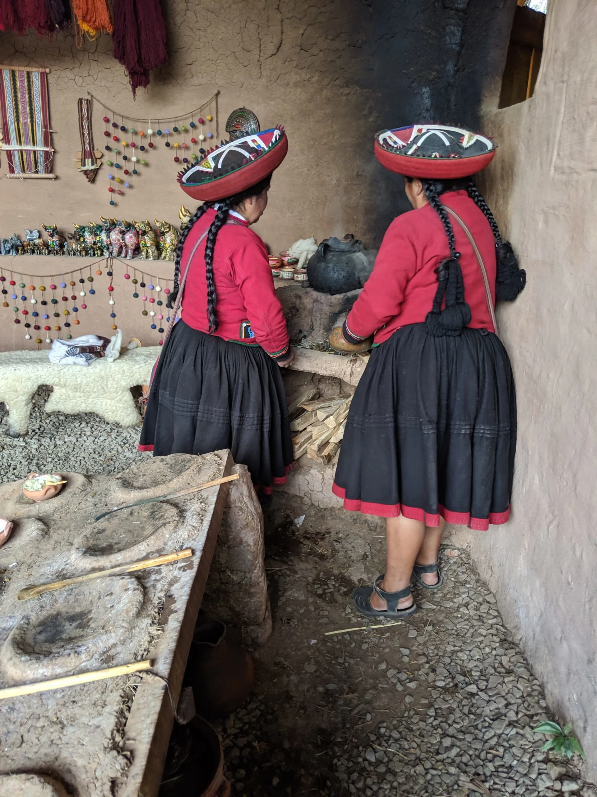 Peruvian women in traditional dress stoking a wood fired stove.