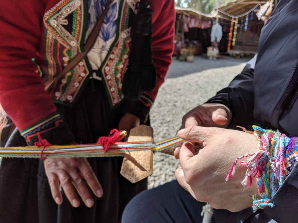 A close-up of hands of a tourist weaving under the instruction of a professional weaver.