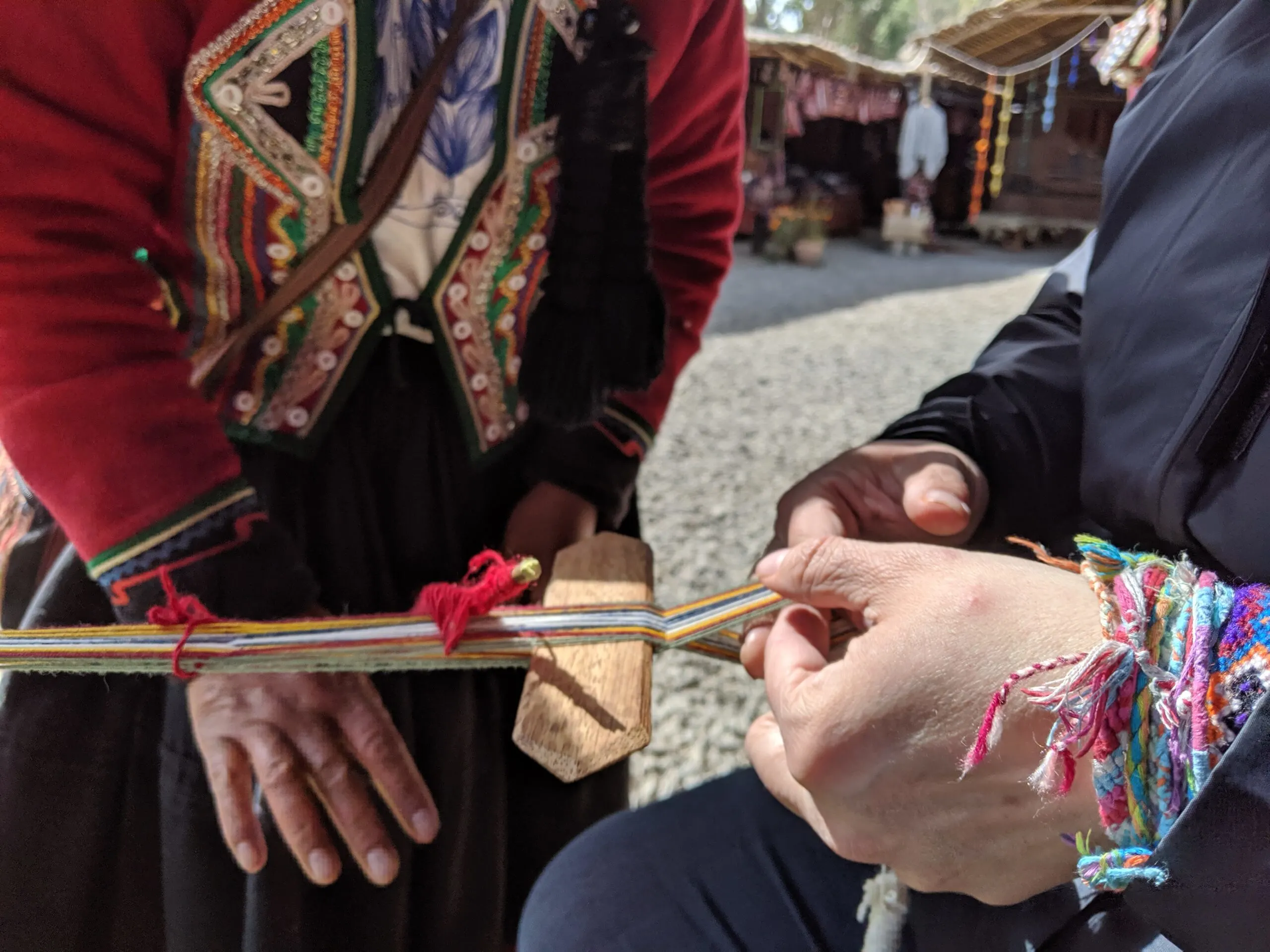 A close-up of hands of a tourist weaving under the instruction of a professional weaver.