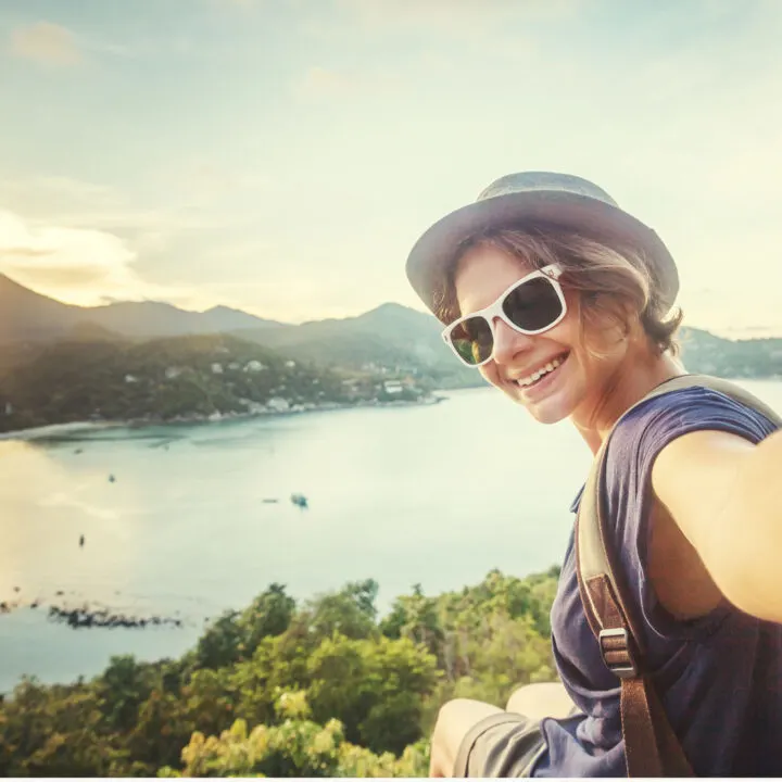 A photo of a woman taking a selfie with a scenic backdrop with the words
