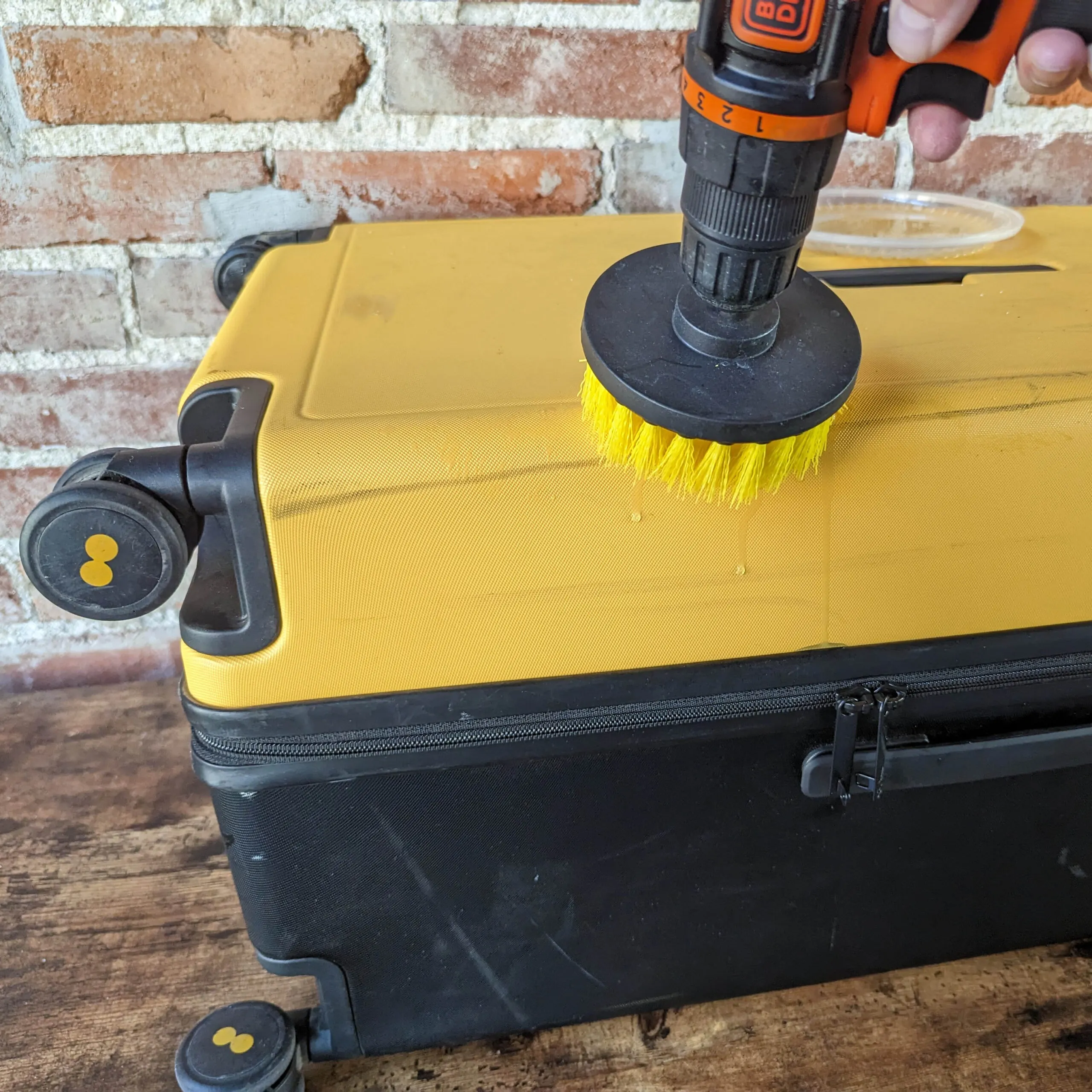 A drill brush scrubbing a hard shell suitcase