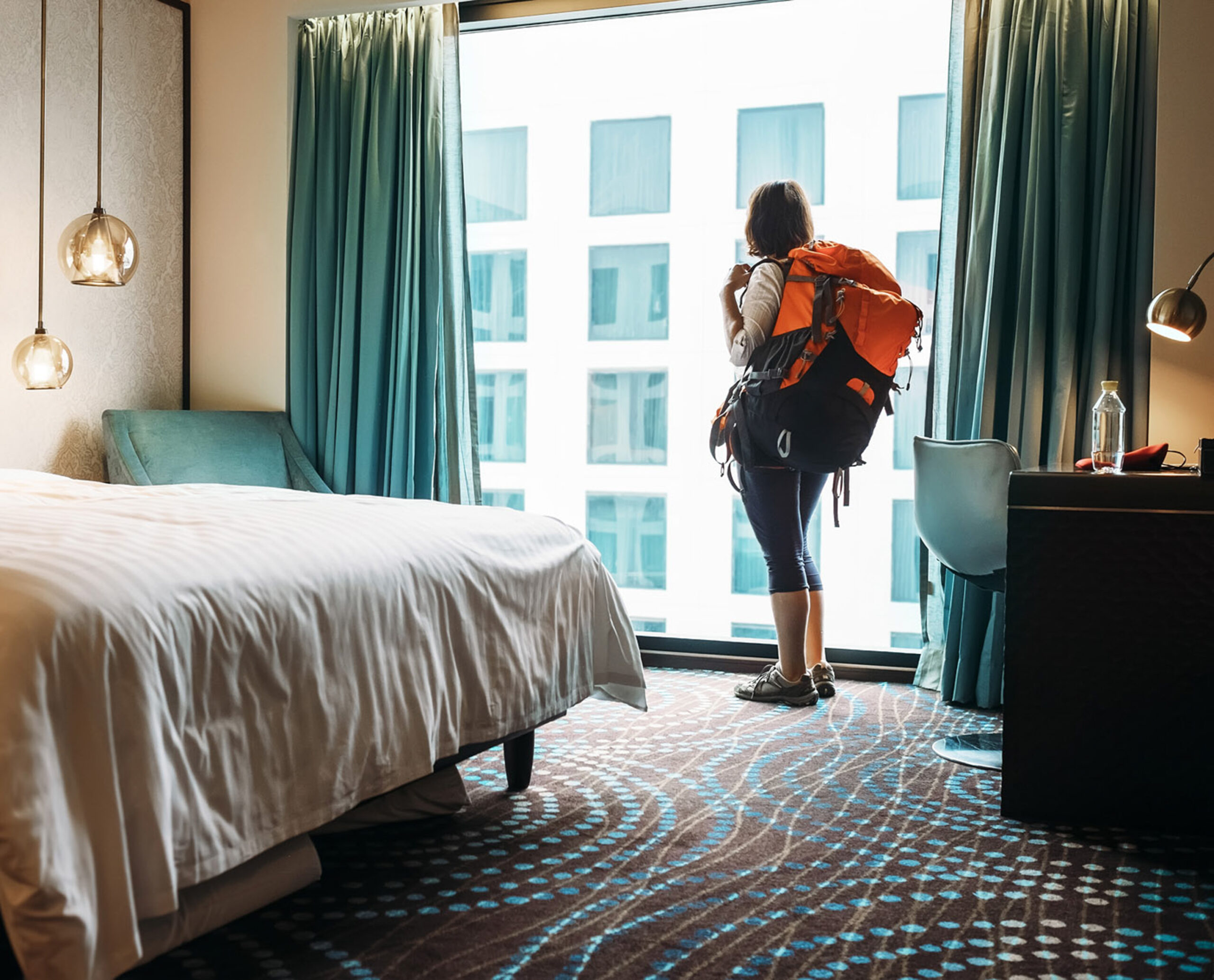 A traveler looks out a window wearing a backpack.