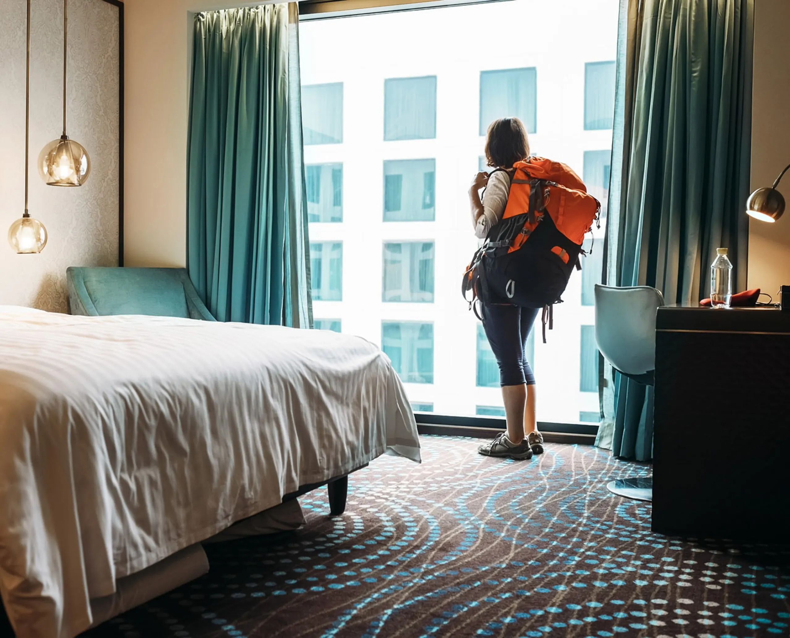 A traveler looks out a window wearing a backpack.