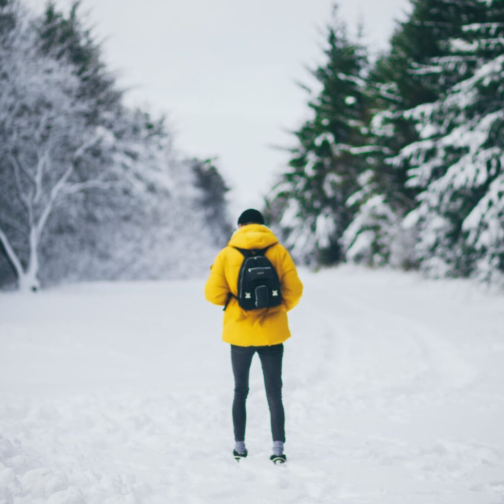 Man in yellow jacket alone in the snow - if you find yourself planning to spend christmas solo, consider booking a ticket to these destinations for a christmas solo travel adventure.