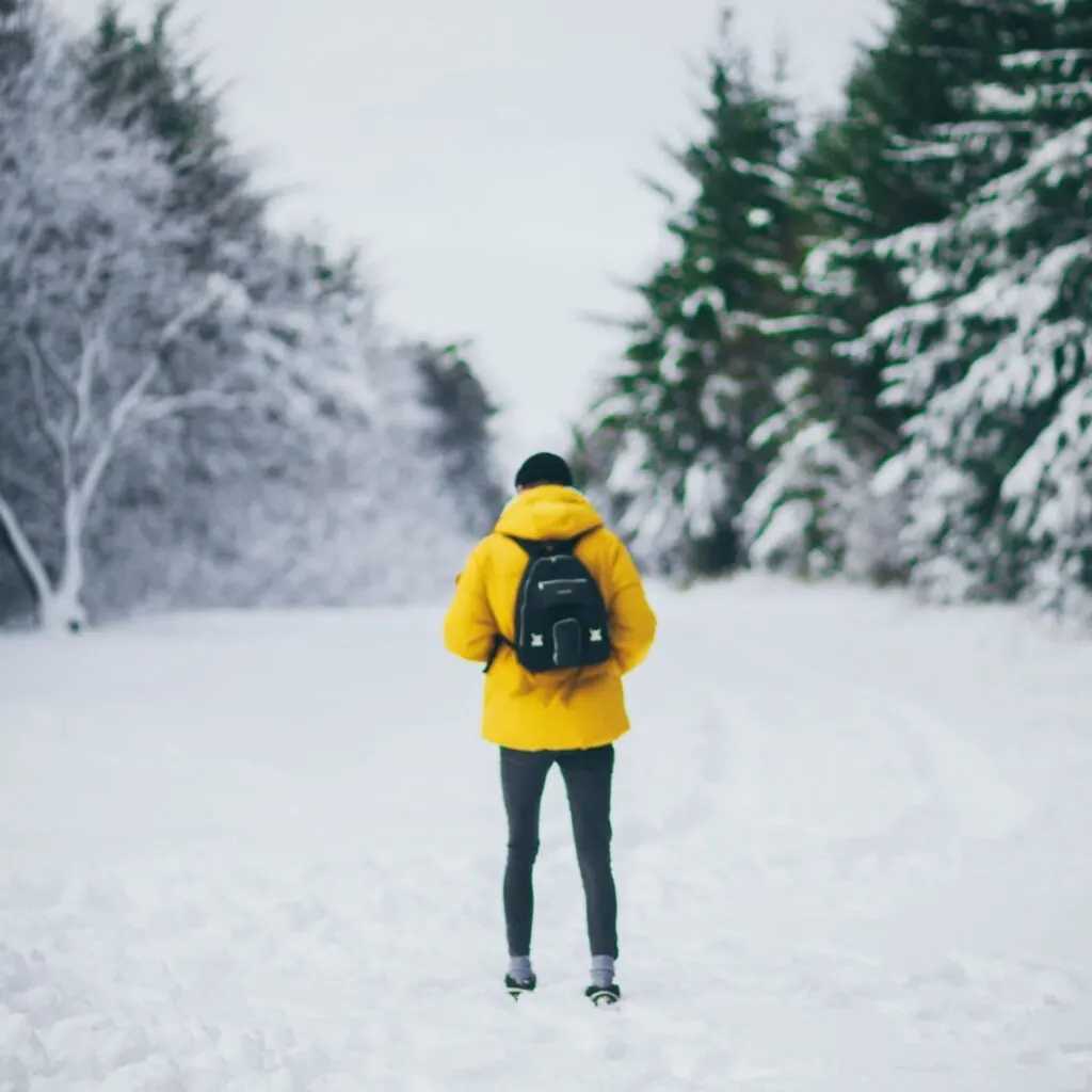 Man in yellow jacket alone in the snow - if you find yourself planning to spend christmas solo, consider booking a ticket to these destinations for a christmas solo travel adventure.