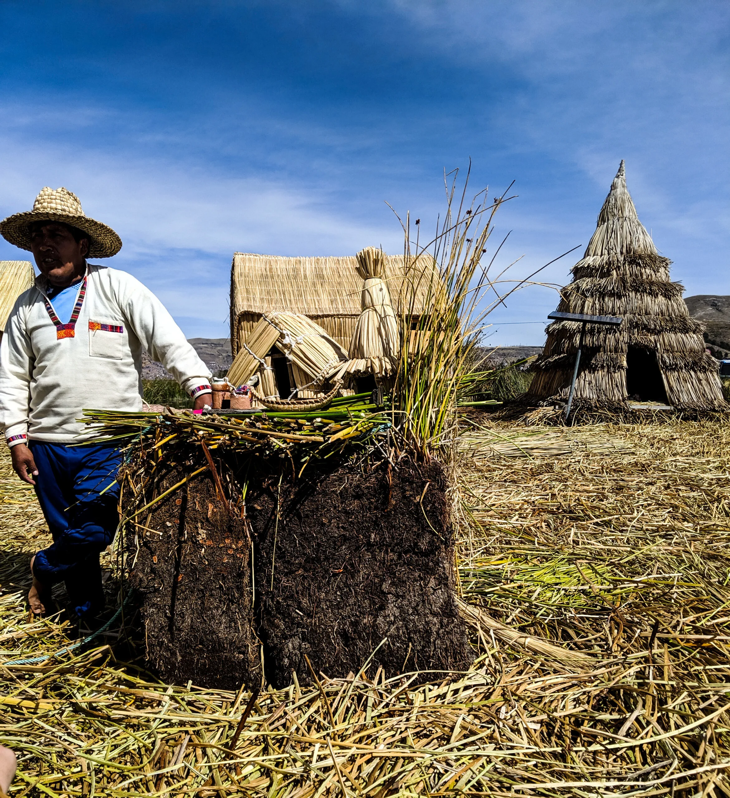 A native tour guide poses with a cross-section of a floating island, with a modern solar panel in the background.
