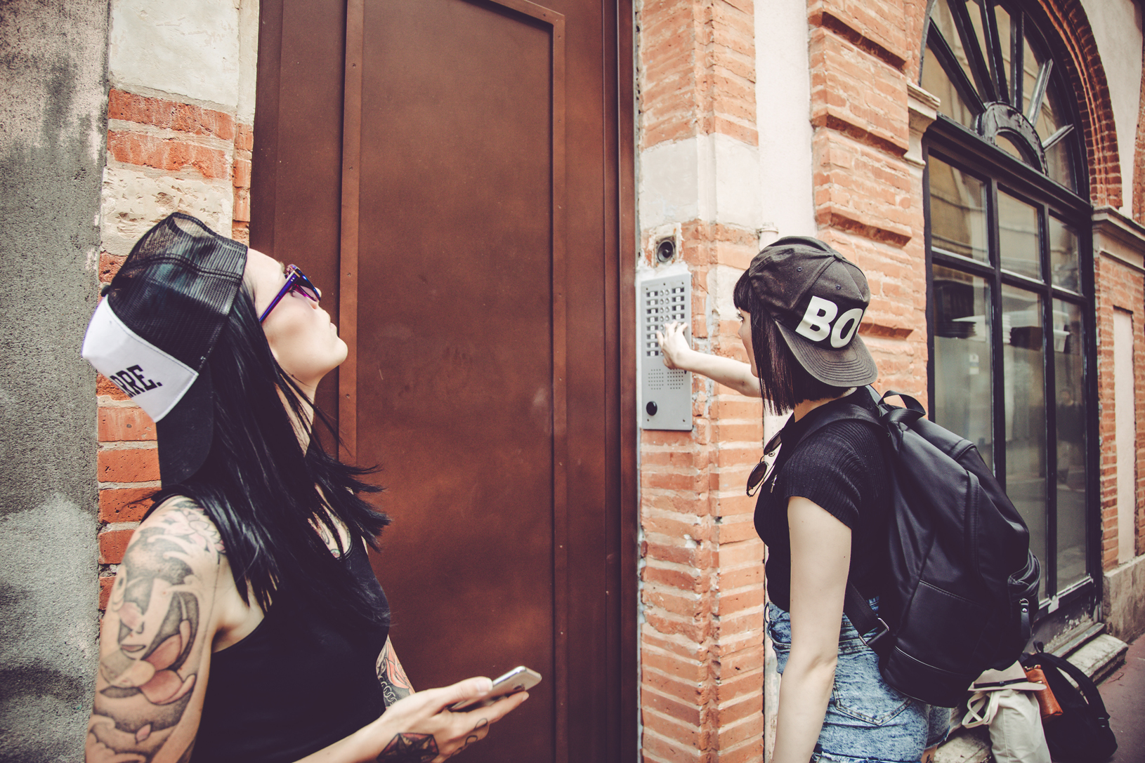 Two women ring a doorbell in an older looking urban neighborhood.