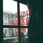 A woman looks out a window at the pike place market sign and christmas decorations