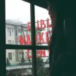 A woman looks out a window at the pike place market sign and christmas decorations