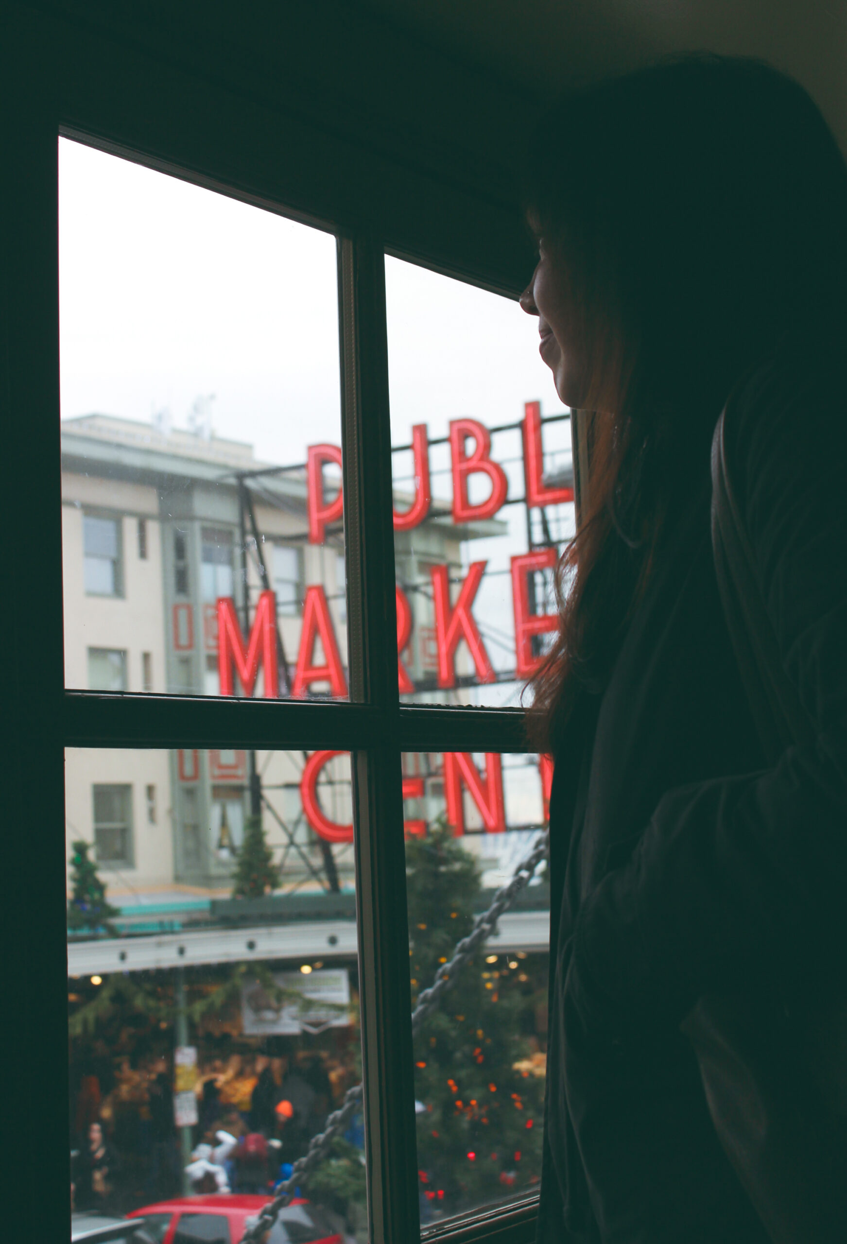 A woman looks out a window at the pike place market sign and christmas decorations
