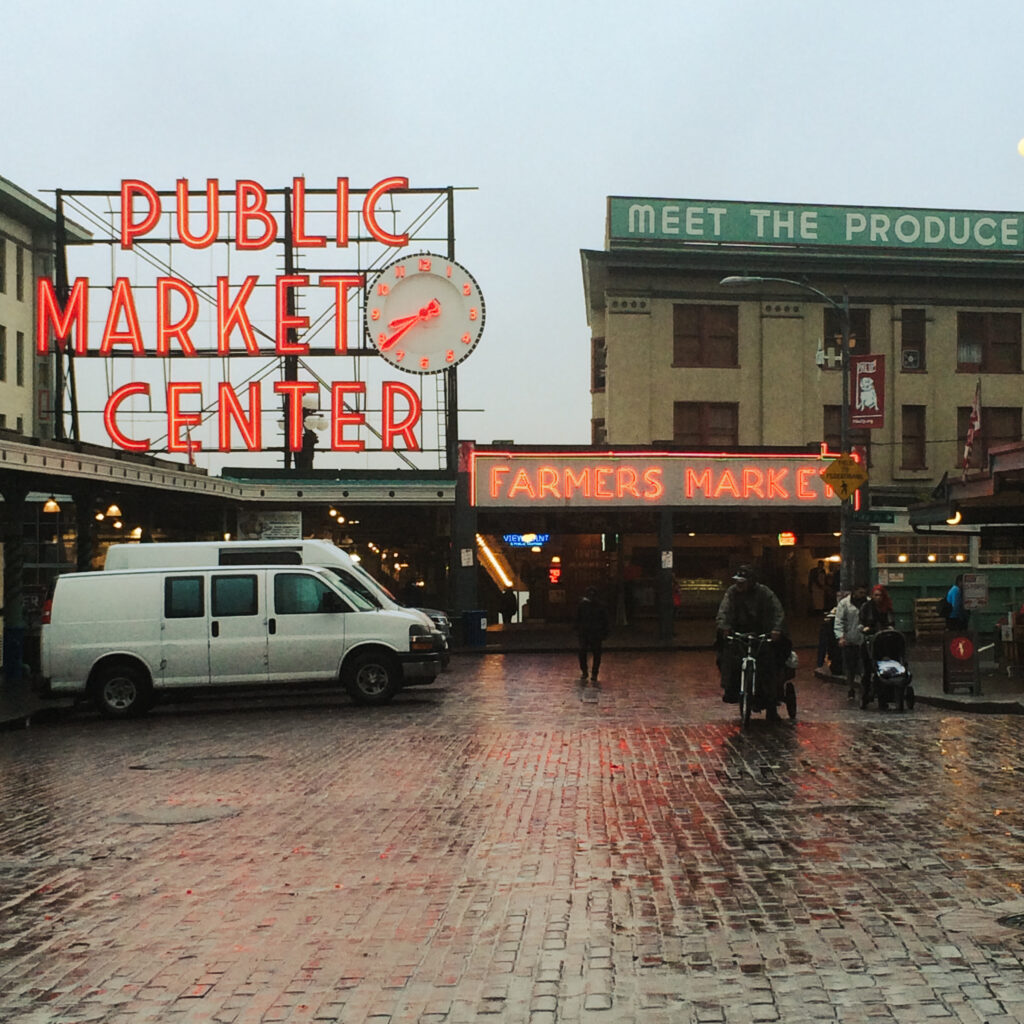 Pike place market on an overcast day with wet bricks and neon signs.