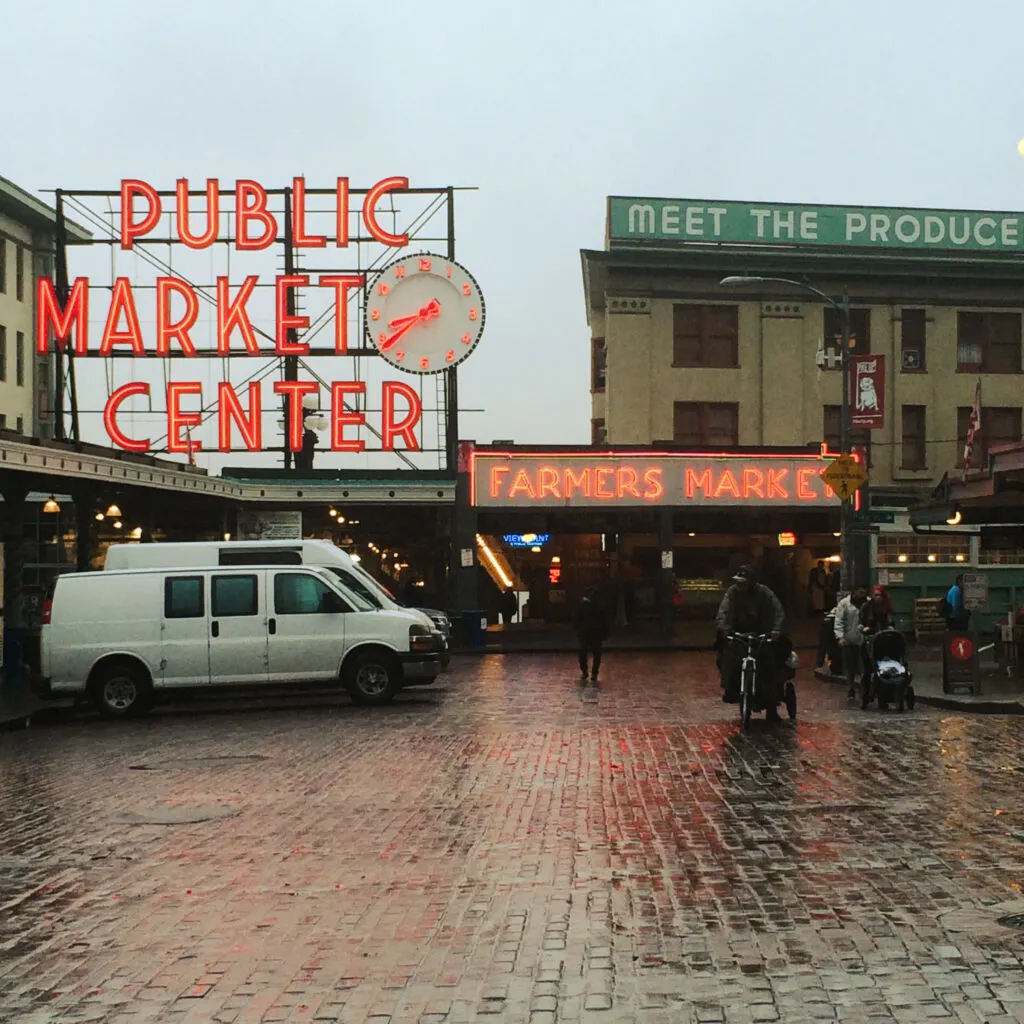 Pike place market on an overcast day with wet bricks and neon signs.