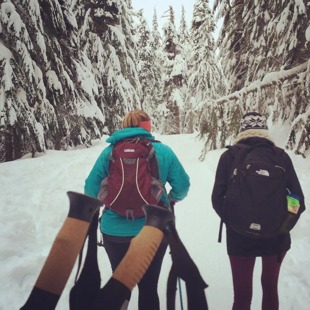 Two women hiking into a snow-covered woods.