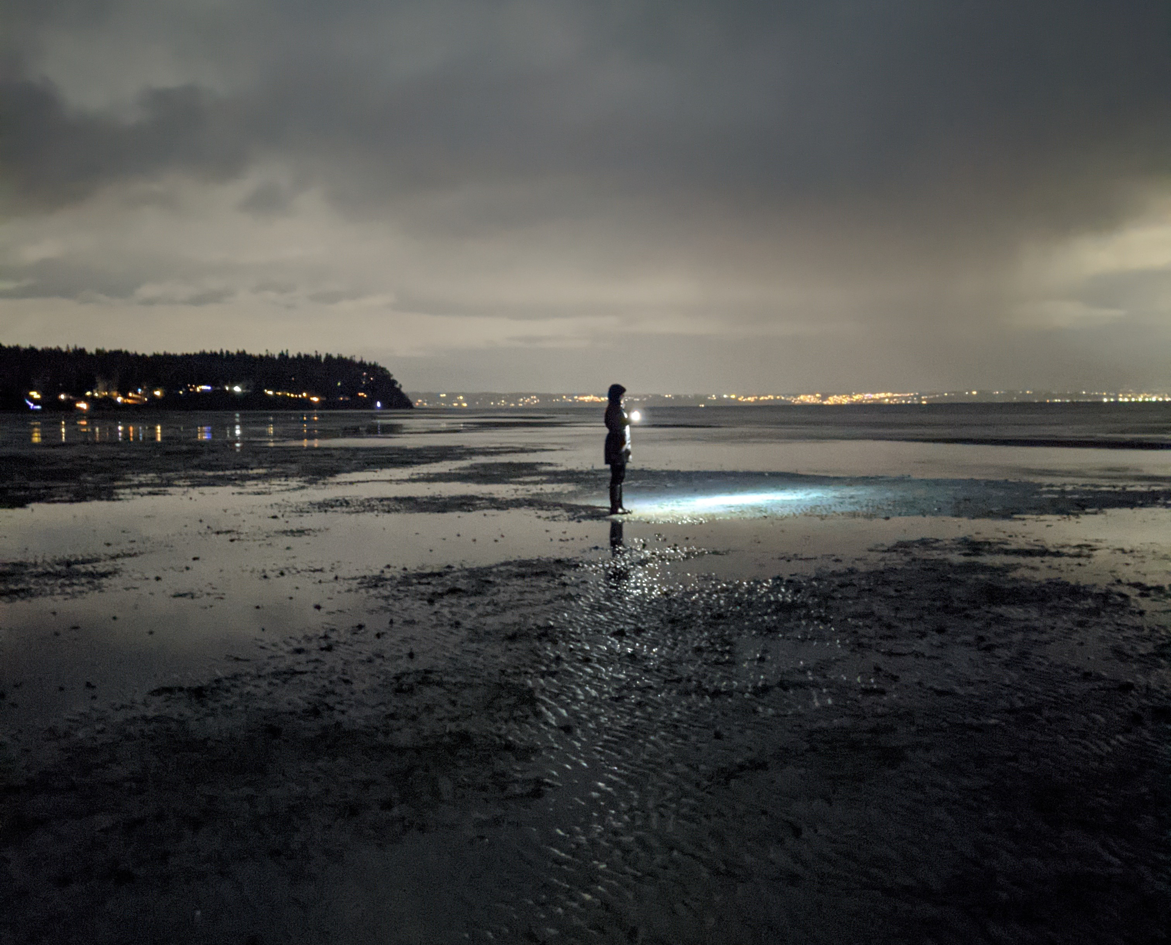 A person stands on tight flats in the dark with the city of seattle in the background