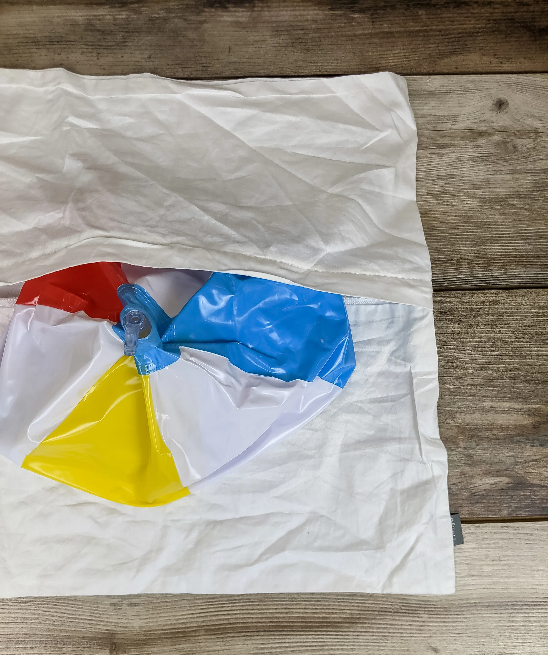 An uninflated beach ball being inserted into a cotton pillowcase to form a diy travel pillow.