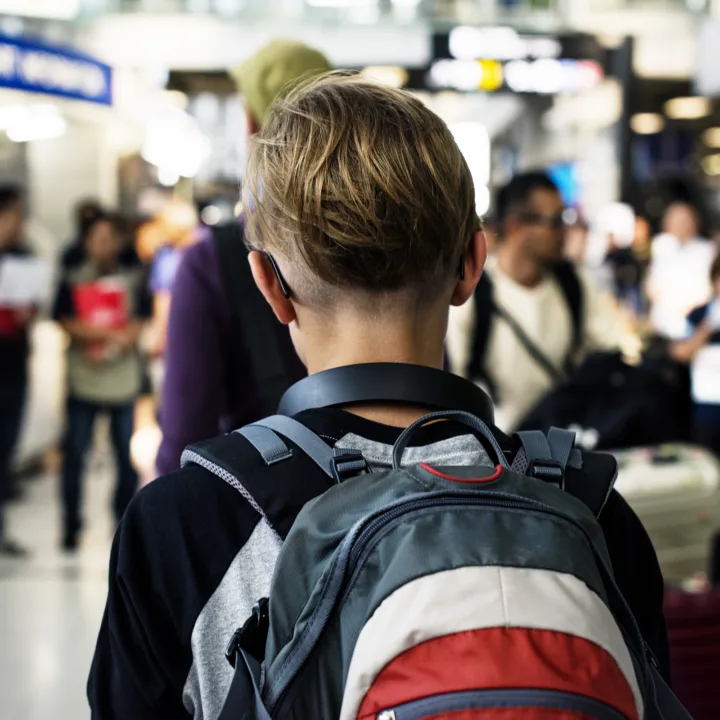 A young person with short hair walks through an airport with a backpack.