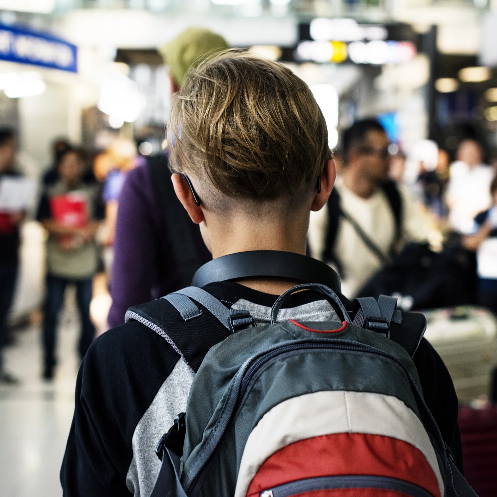 A young person with short hair walks through an airport with a backpack.