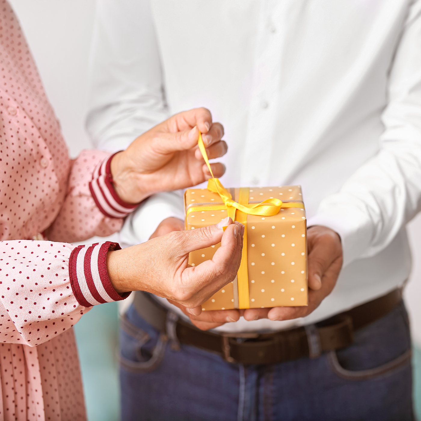 A woman's hands open a gift held by a man in a white shirt.