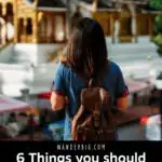 Text reading six things you should always carry while traveling overlaid over an image of a woman wearing a backpack with her back turned to the camera as she looks at a cultural building.