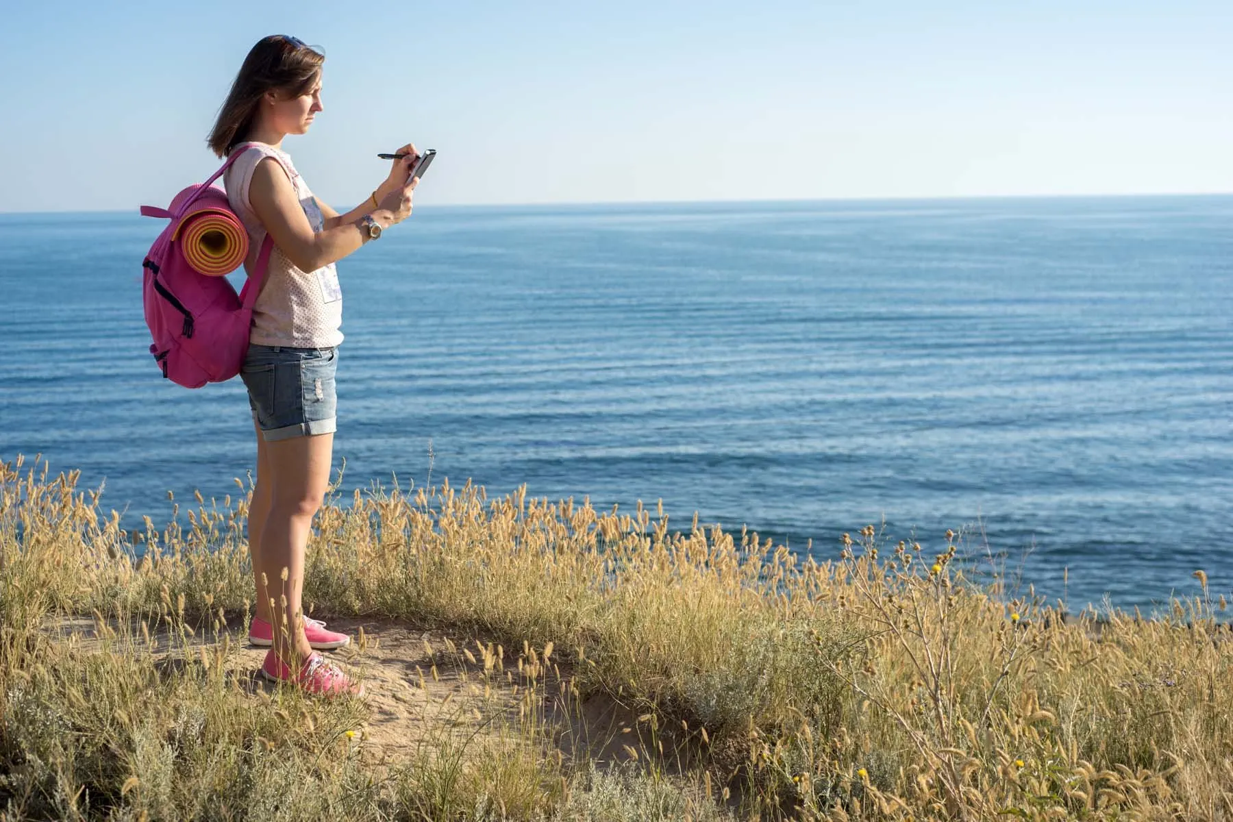 A woman stands on a beach and takes a photo of the water.