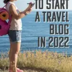 Text reading 15 steps to start a travel blog in 2022, overlaid over an image of a woman on the shoreline taking notes on a digital device.