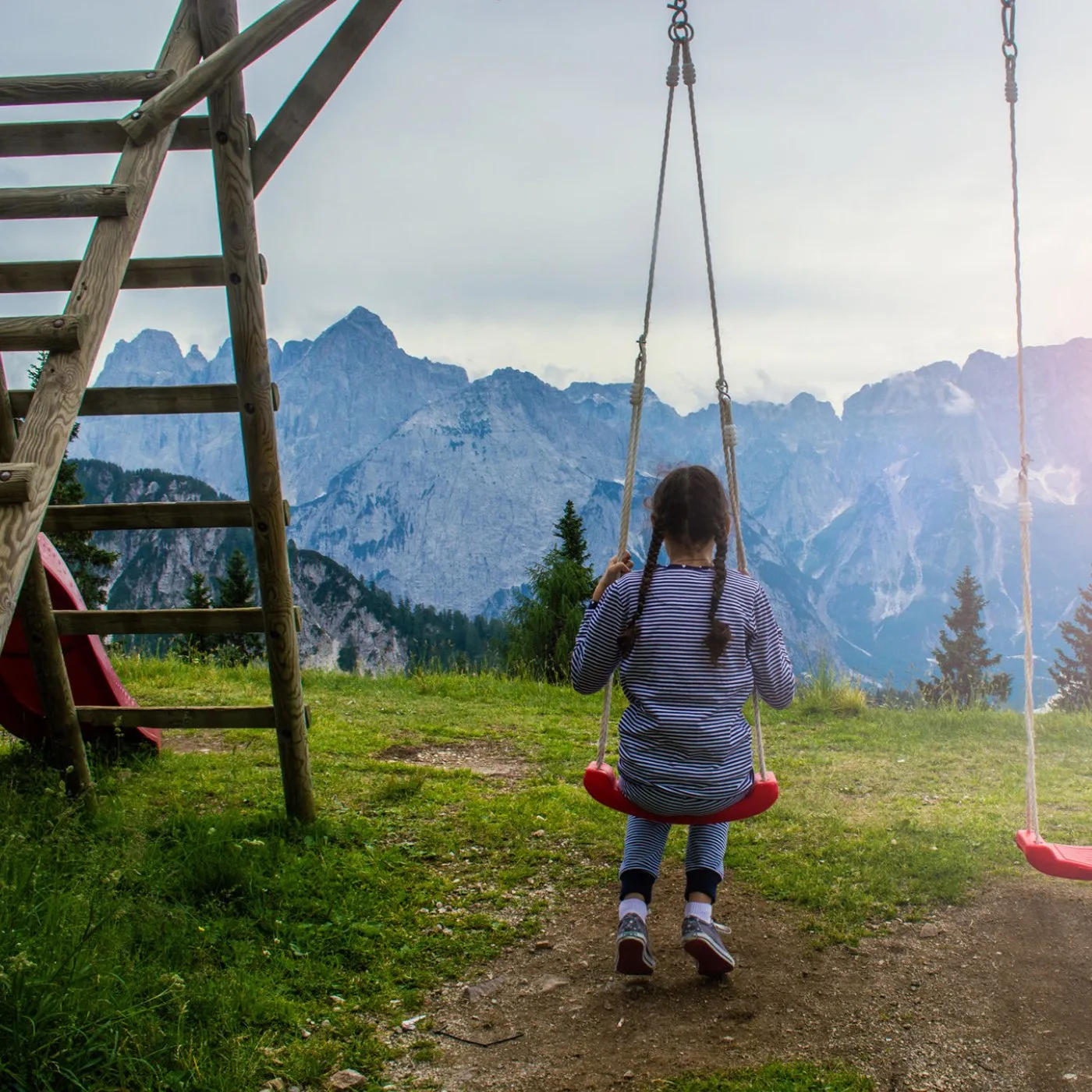 A child on a rustic swingset with mountains in the background.