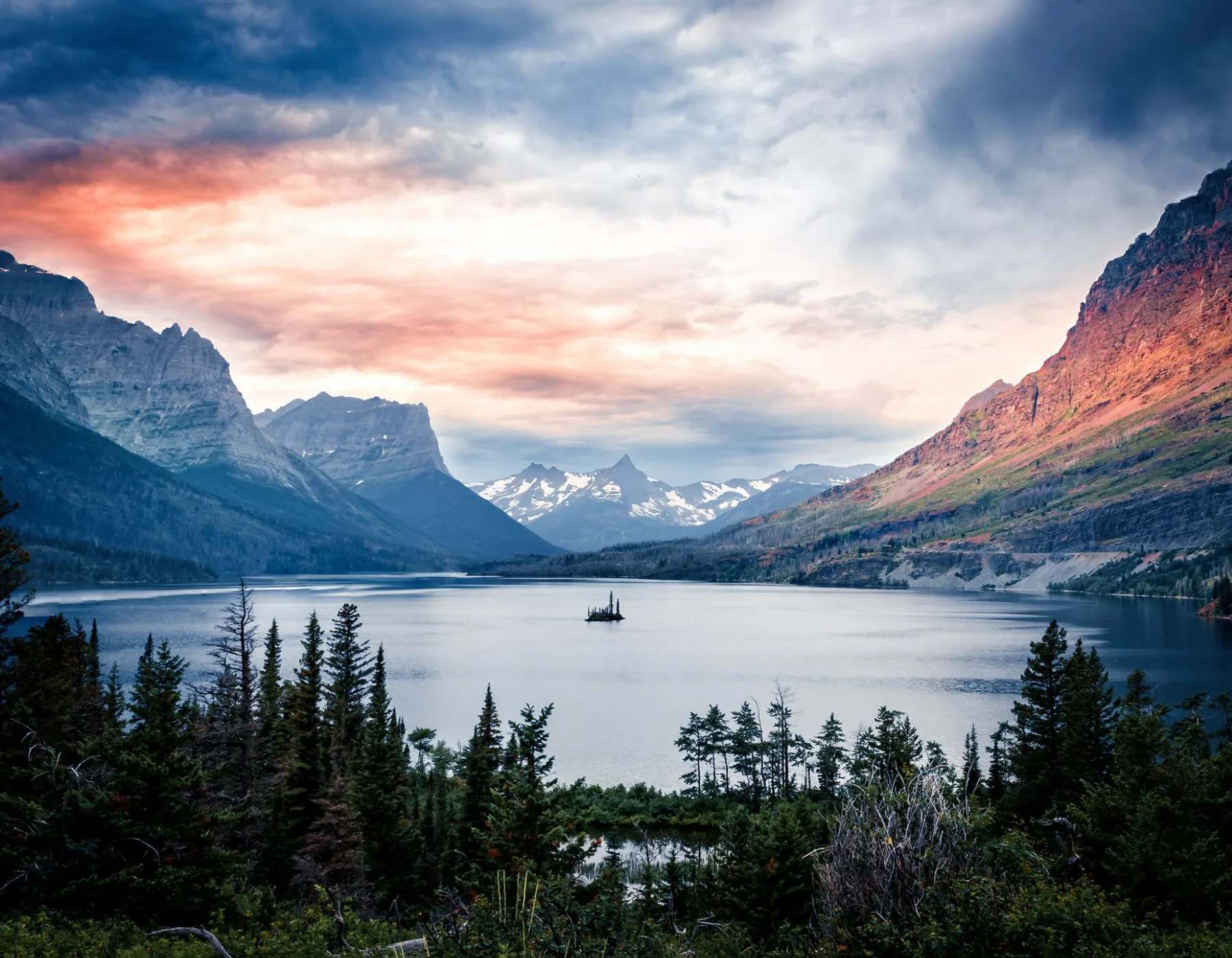 A photo of glacier national park showing a glacial lake with an exposed island in the center.