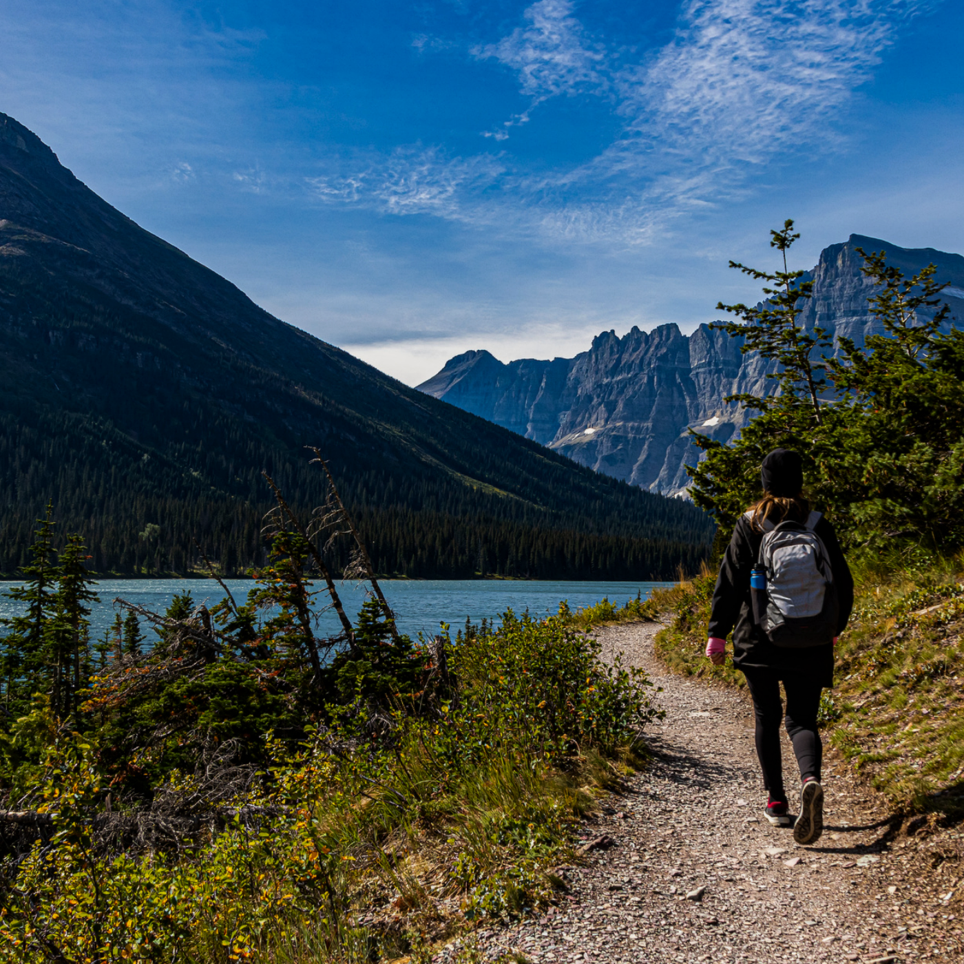 A photo of glacier national park with a person walking down a trail.