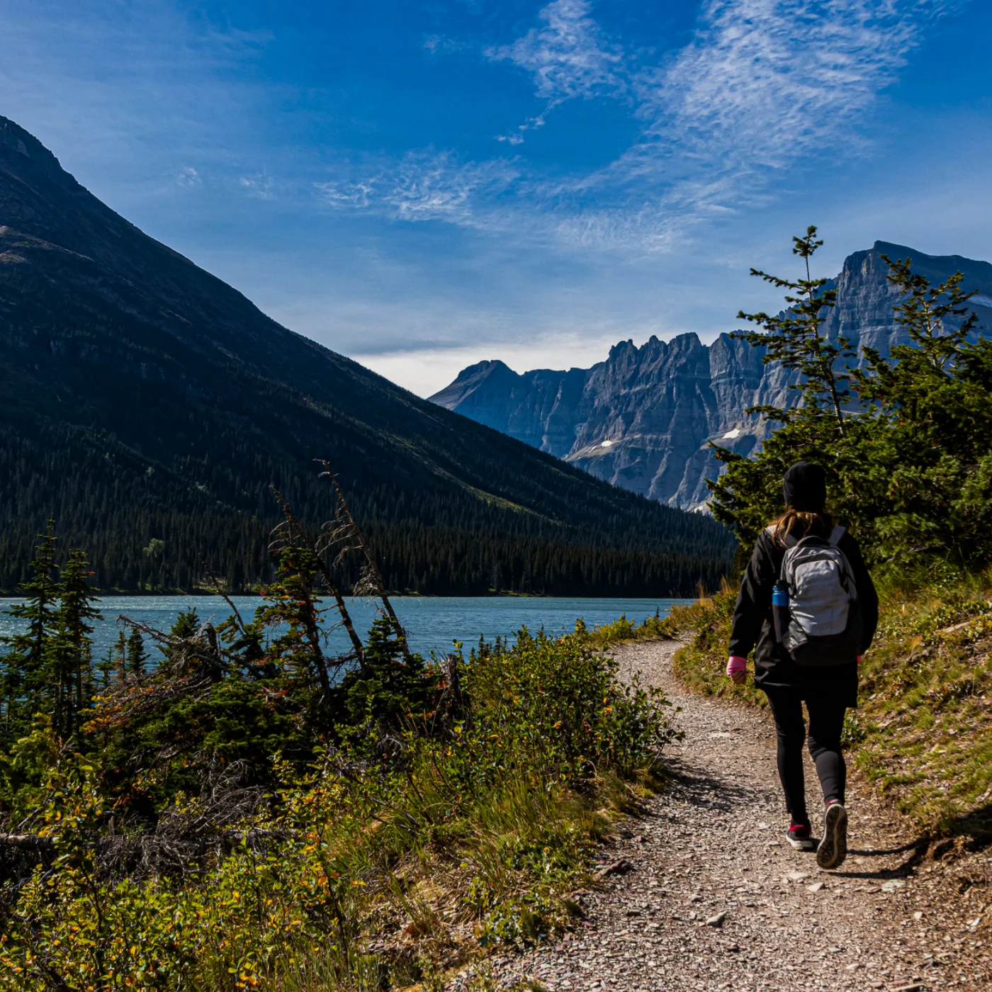 A photo of glacier national park with a person walking down a trail.