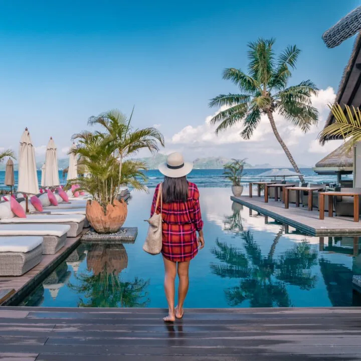 A woman stands on the edge of a hotel pool near a waterfront, with the test overlay how to plan luxury travel on a budget.