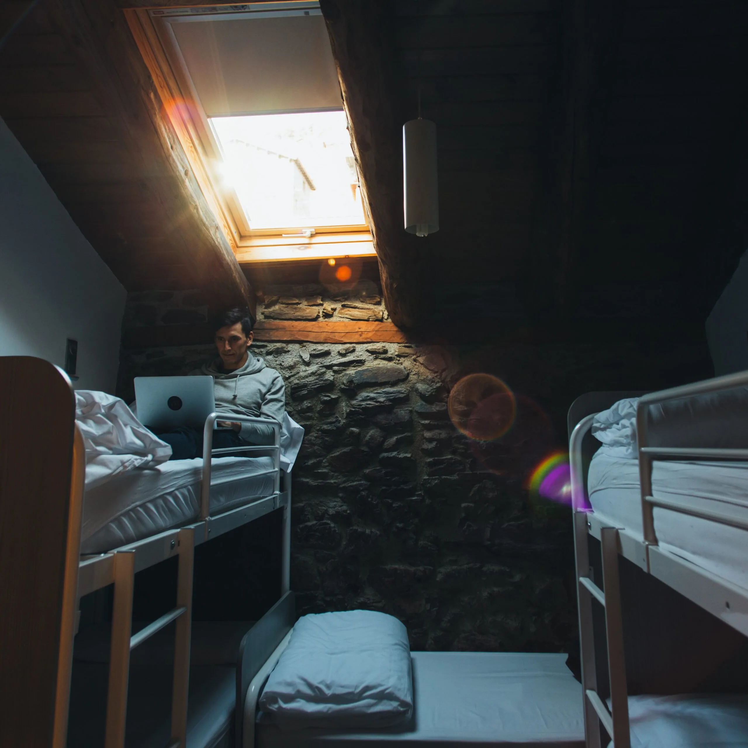 Man sitting on bunk bed in dark hostel dorm room.