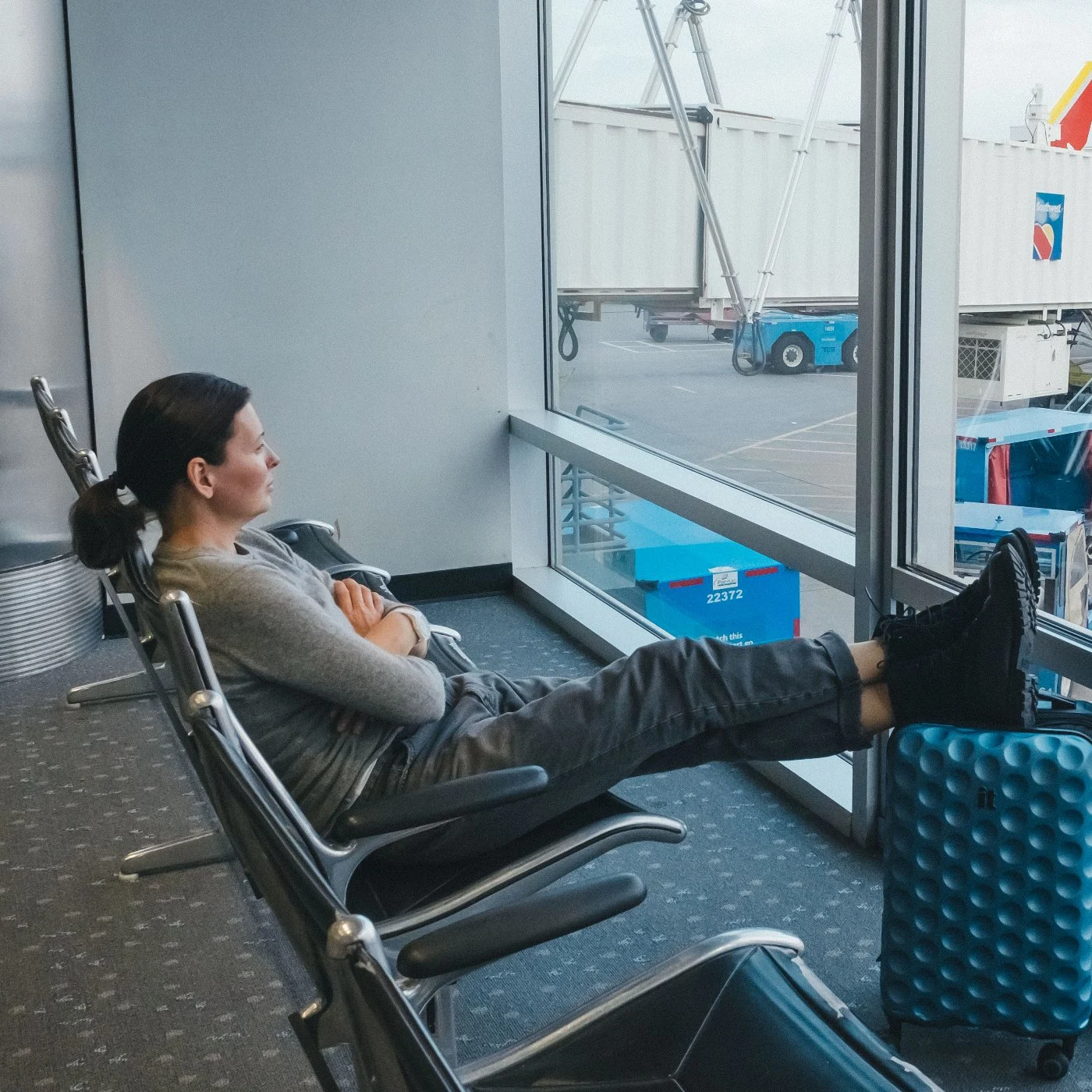 Woman in airport rests with feet elevated on suitcase.