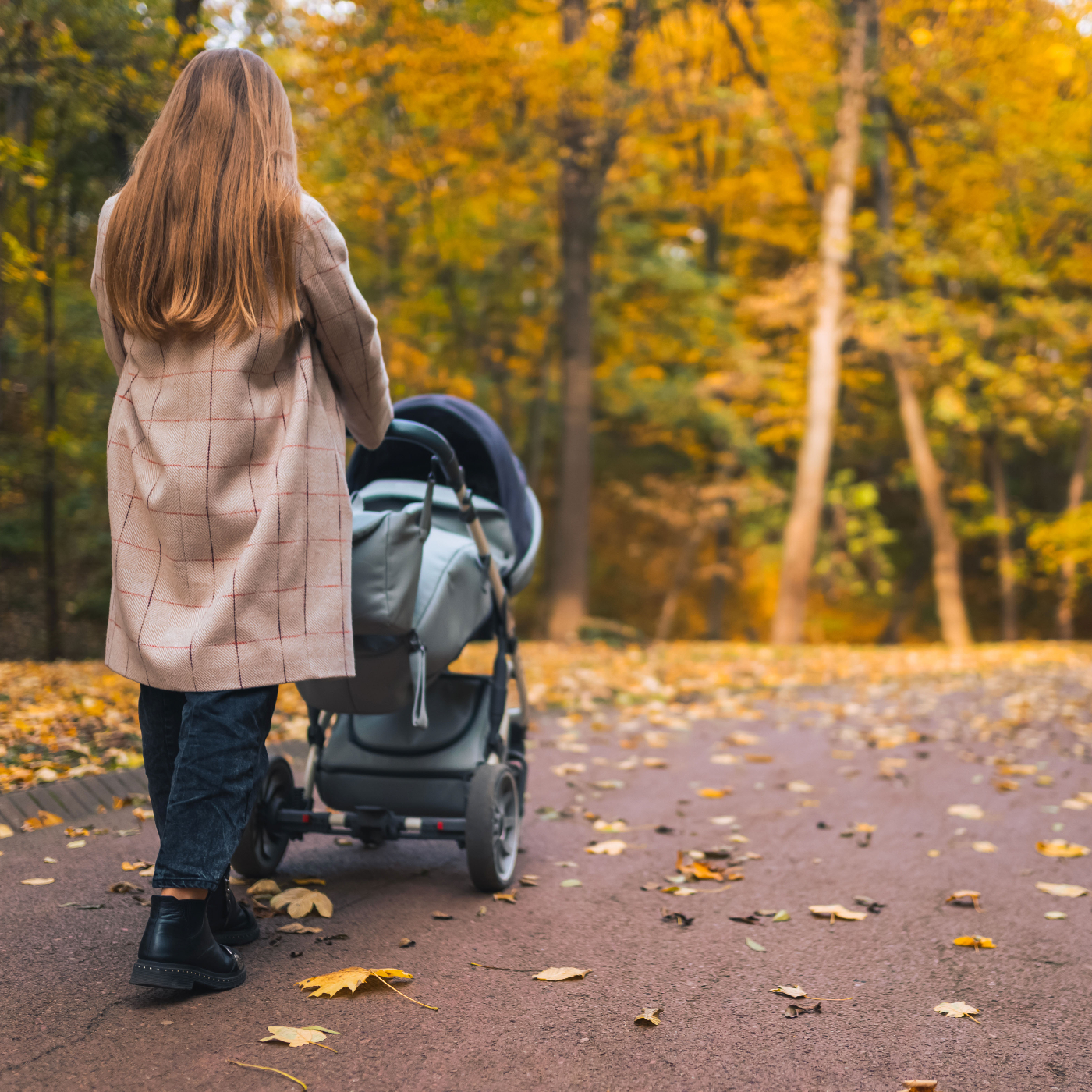 An au pair pushes a stroller through a park.
