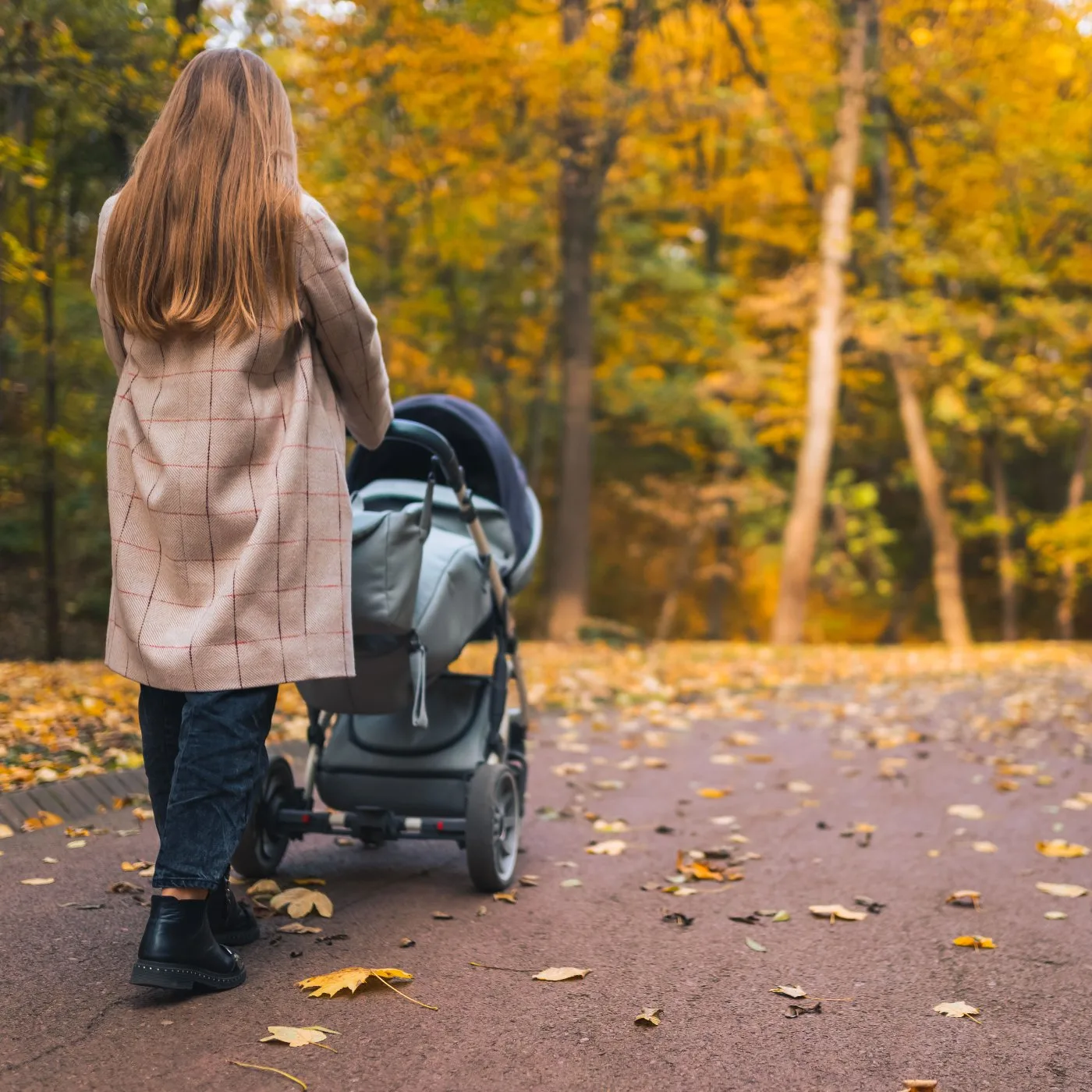 An au pair pushes a stroller through a park.